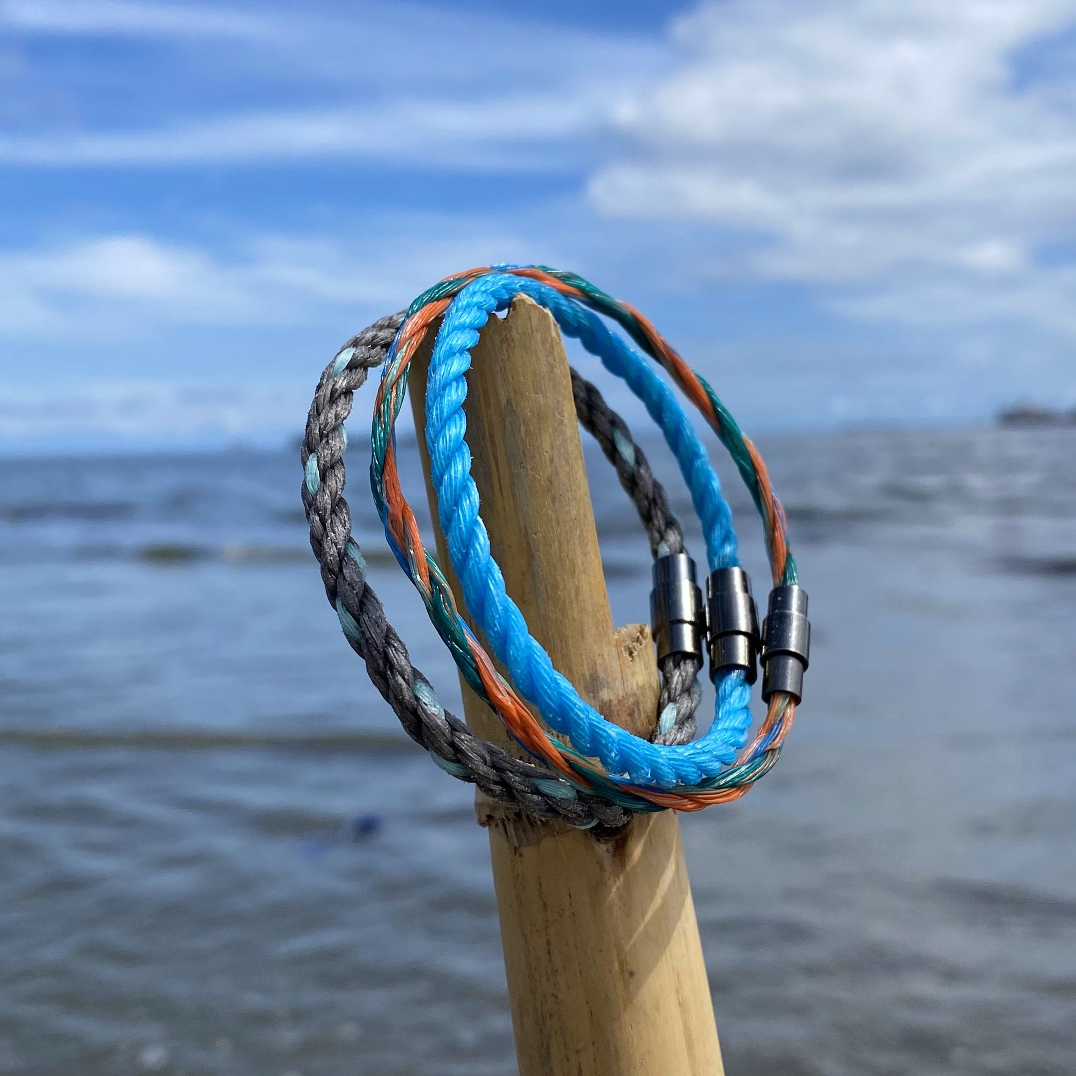 3 SeaSweeper unbreakable bracelets being held up in front of the beach by bamboo.